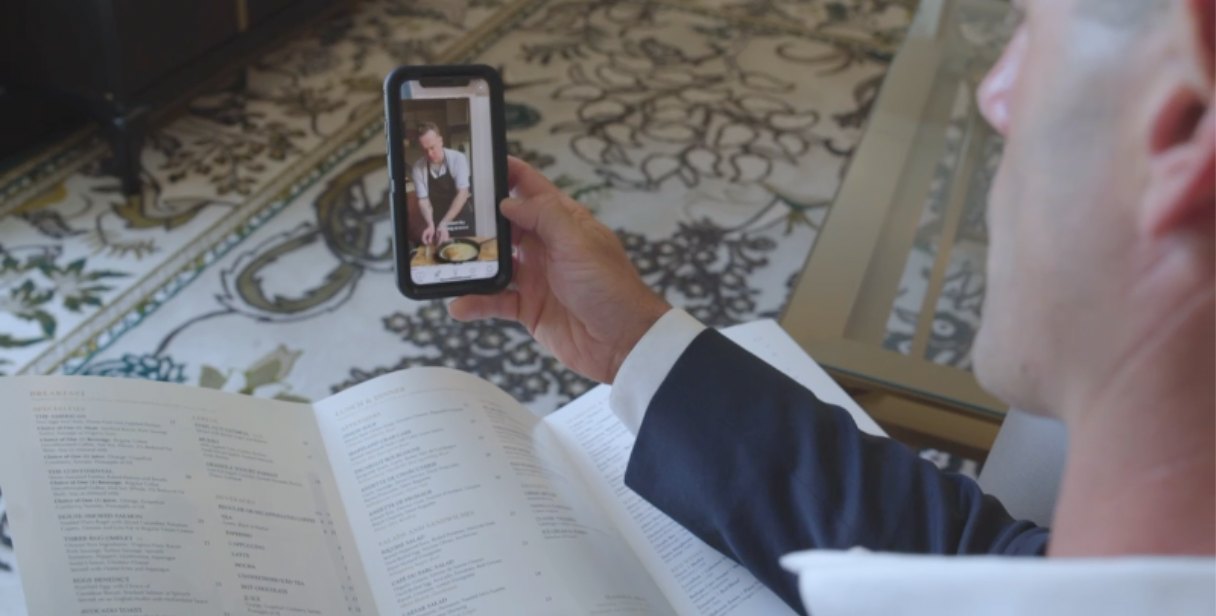 A guest points a phone at a breakfast menu and watches the chef prepare the dish